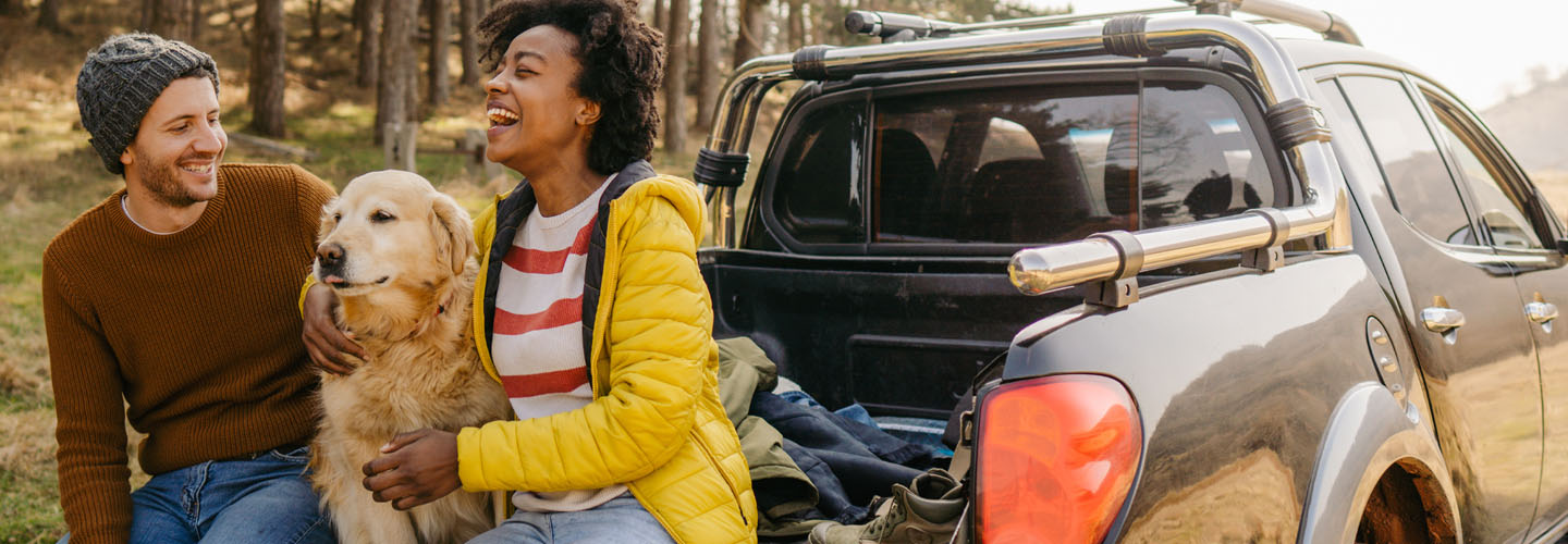 man and woman laughing with dog sitting in between them in the back of a truck